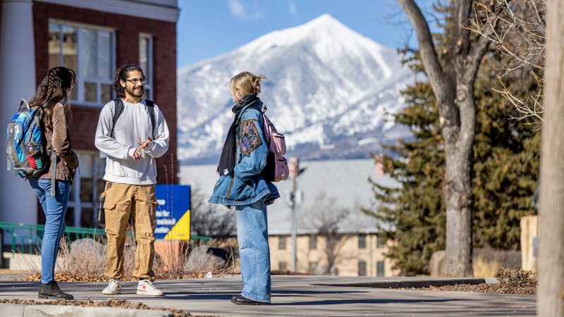 Students standing outside talking with snow capped mountains in the distance