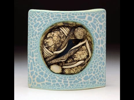 Light blue ceramic square with bone-colored abstract shapes in the center. By student Victoria Vick.