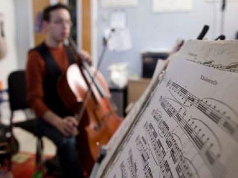 Closeup of music sheet and student with instrument in the background.