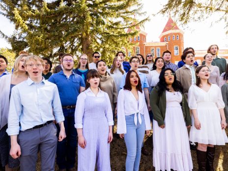 Shrine of the ages choir singing in front of Old Main, dressed in informal blue and white street clothes.