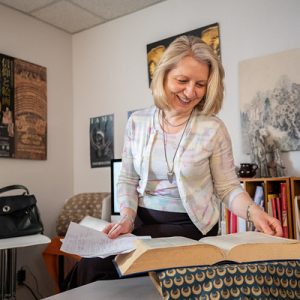 Dr. Gulacsi reviews a text in her office on campus. She stands in front of a large open book.