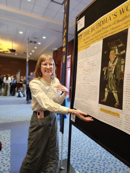 A blonde woman gestures toward her poster which shows a male translator from ancient China with text on a white and yellow background.