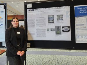 A woman in a black suit stands in front of a blue research poster.