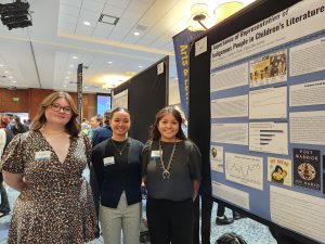 Three women stand in front of a research poster
