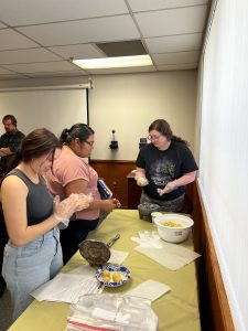 Students in CCS 201 create corn tortillas. Several students handle corn wearing gloves. 