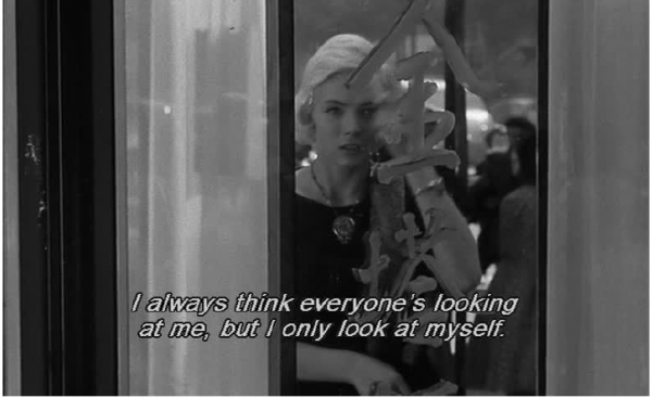in a clip froma black and white film, a Blonde woman looks into a window, wearing a 1960's style dress, text on image reads "I always think everyone is looking at me, but I only look at myself."
