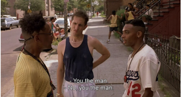 three young men stand in summer street, two black and one white, text on screen reads" "You the man, No, you the man"