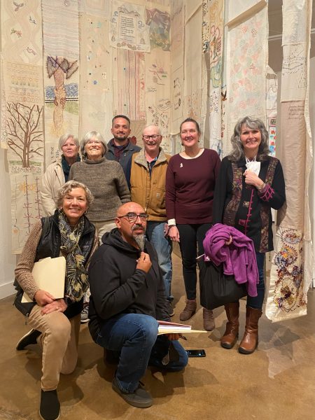Professor Coleman with participants in her archiving workshop in November in the main gallery of Coconino Center for the arts. In the background are wall hangings from the exhibit and there are 7 participants of varying ages.