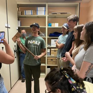 A student holds NAU's original copper axe while several of their classmates observe