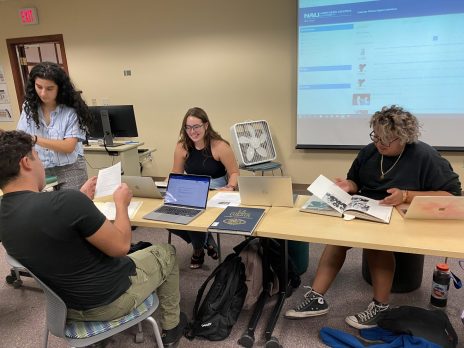 A group of students, along with Dr. Lefty, examining copies of vintage NAU yearbooks.