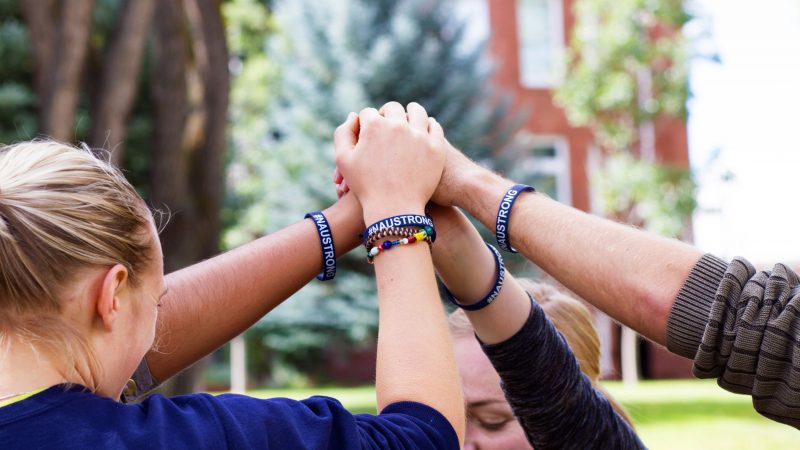 Students hold fists together in the air, wearing matching NAU strong bracelets.