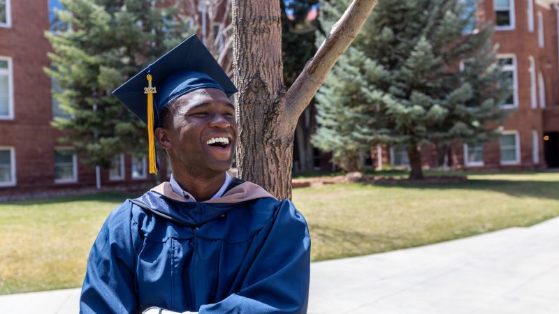 At commencement, a student stands outside with a huge smile in his cap and gown.