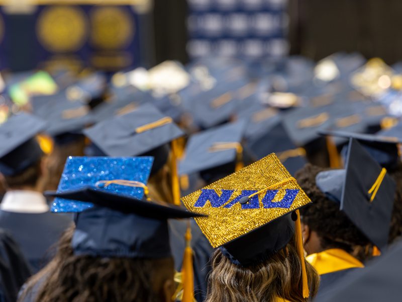 In room full of graduation caps, a sparkling NAU logo graduation cap shines.