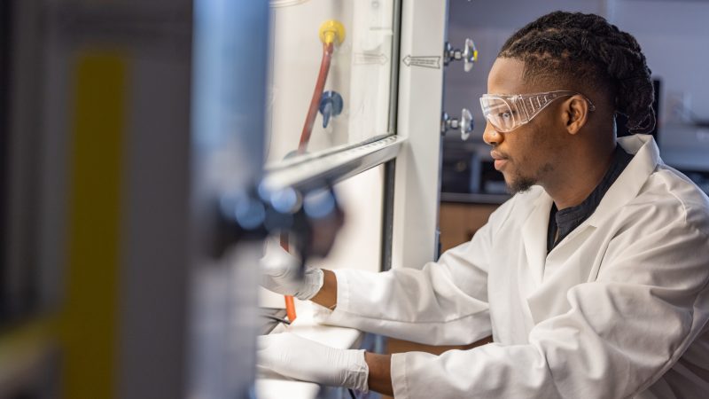 A medical student wearing protective glasses works in a lab.