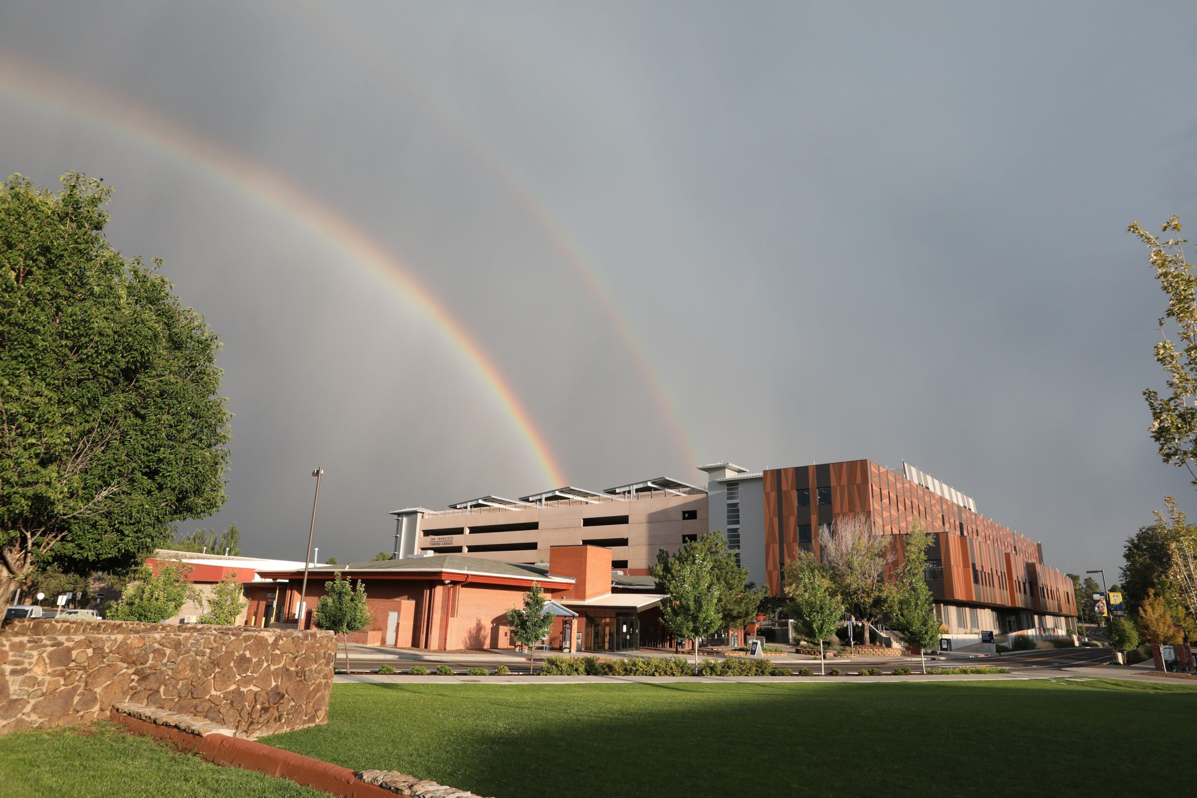 Two rainbows arching over NAU Flagstaff campus buildings against a dark sky.