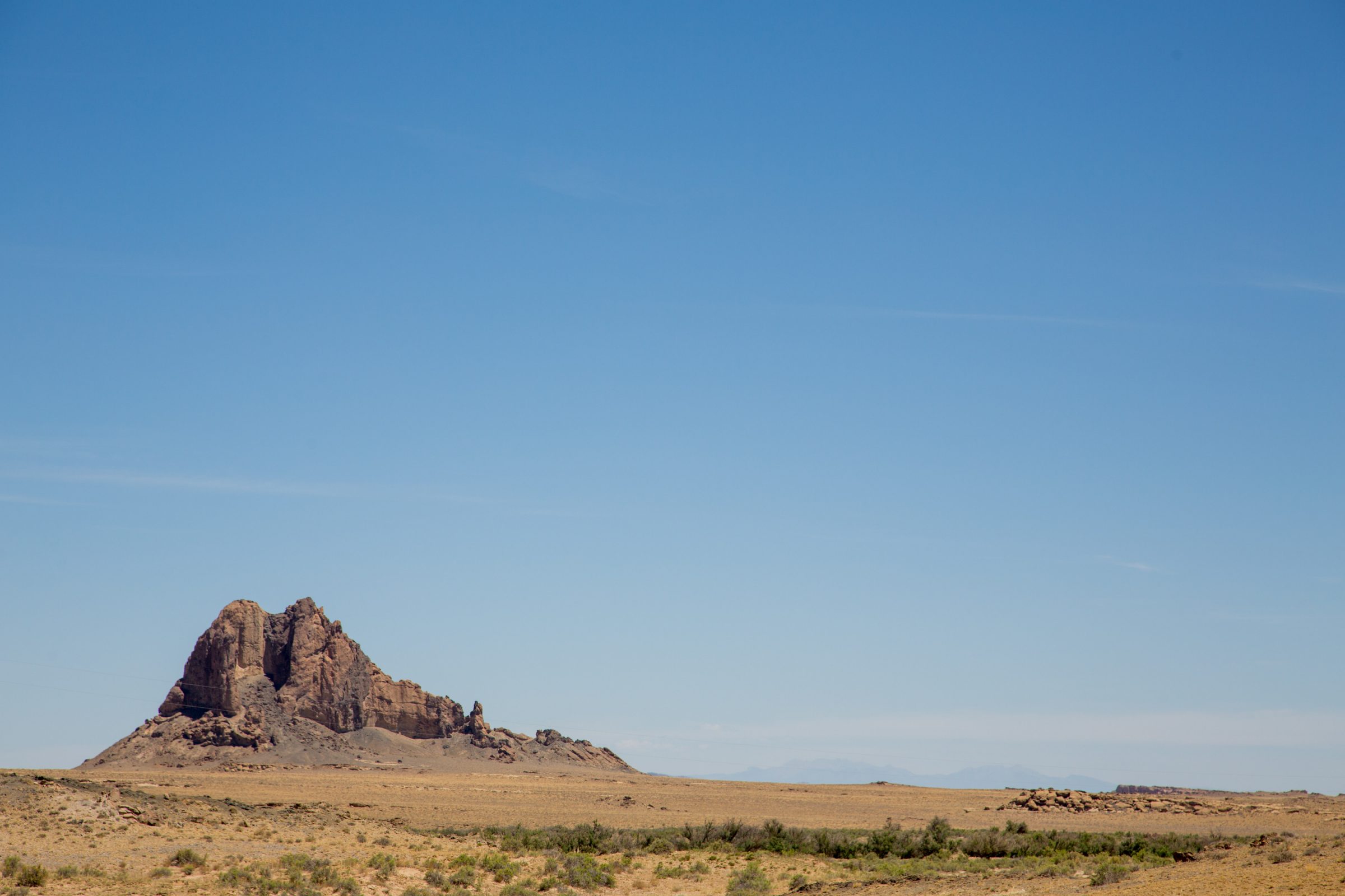 Landscape photo of desert in the foreground, with a rocky bluff off to the side.