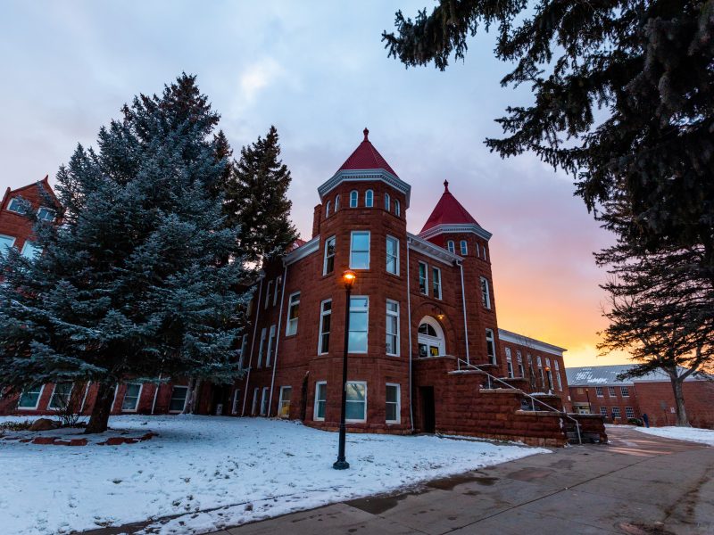 Old Main campus building on a snowy day with a sunset in the background.