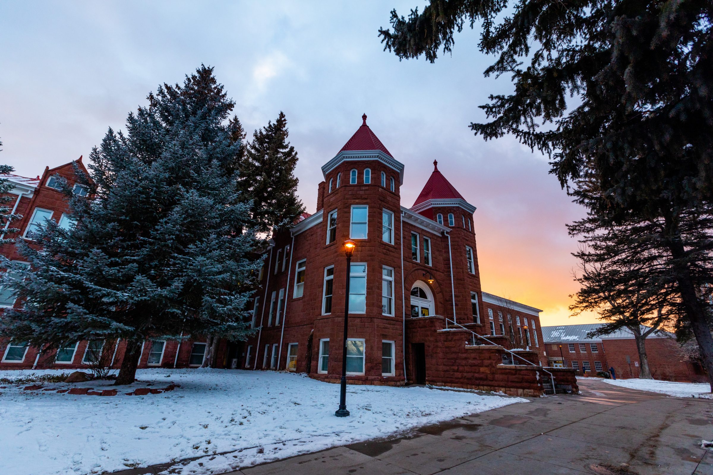 Old Main campus building on a snowy day with a sunset in the background.