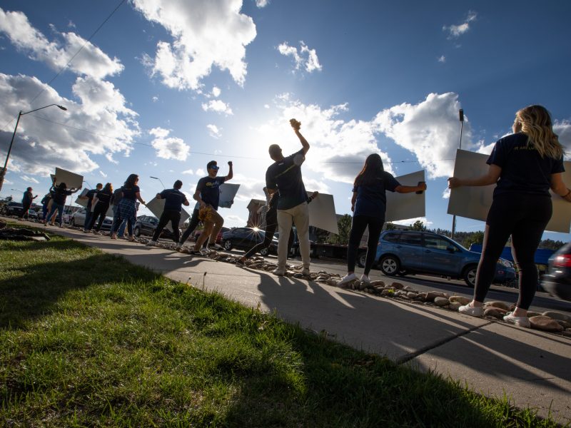 Students standing along a road holding up signs.