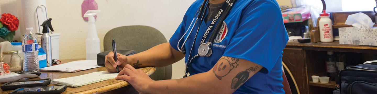 A cropped image of a CHR working for a patient wearing blue scrubs, a stethoscope, and typing.