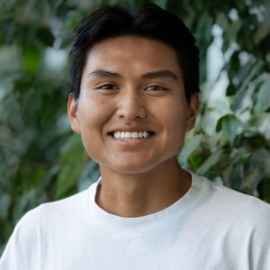 A headshot of Wacey Begay, who has short brown hair, against a green background.