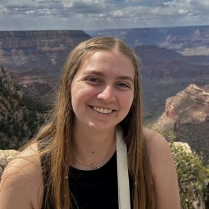 A photograph of Lauren Frick, who has long blonde hair, standing on the rim of Grand Canyon