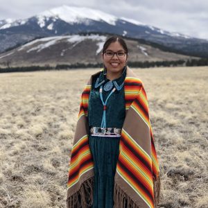 Andria Begay stands wrapped in traditional clothing in front of the sacred peaks.