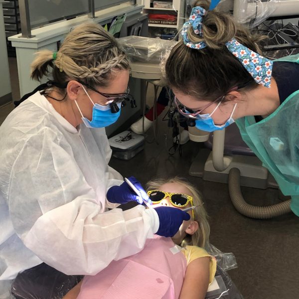 Two dental hygienists cleaning on a child's teeth.