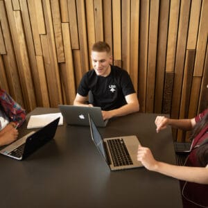 Three students with laptops working at a table.