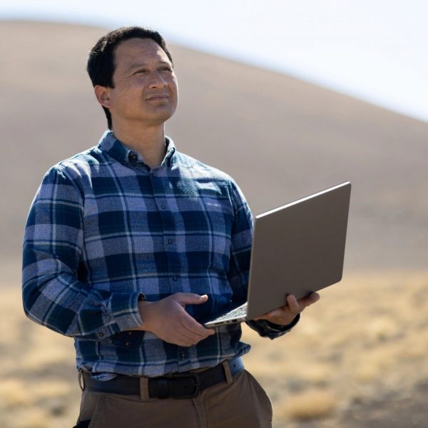 Frank Telles holding laptop computer while doing dust and drought research at study site.