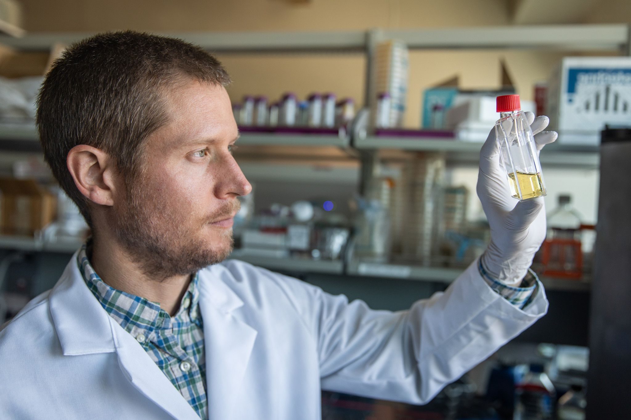 Jason Ladner, in his lab, looking at a vial that has liquid in it.