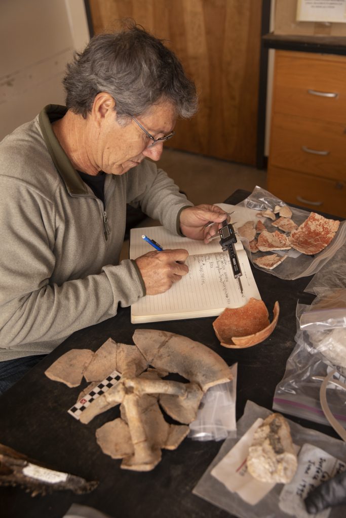 Professor Jaime Awe makes notes after measuring archaeological artifacts.