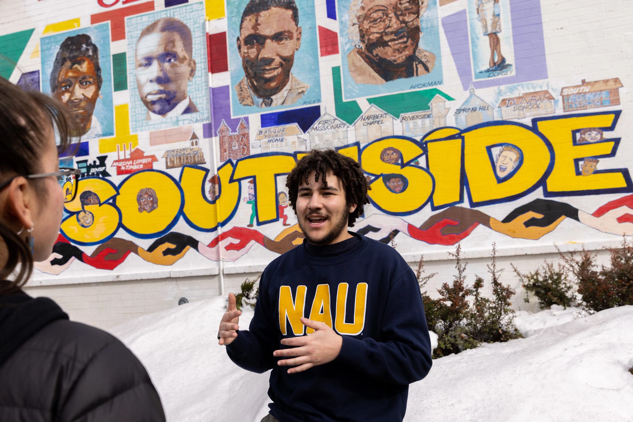 Undergraduate Ty Holliday talking with visitor in front of the Murdoch Community Center mural.
