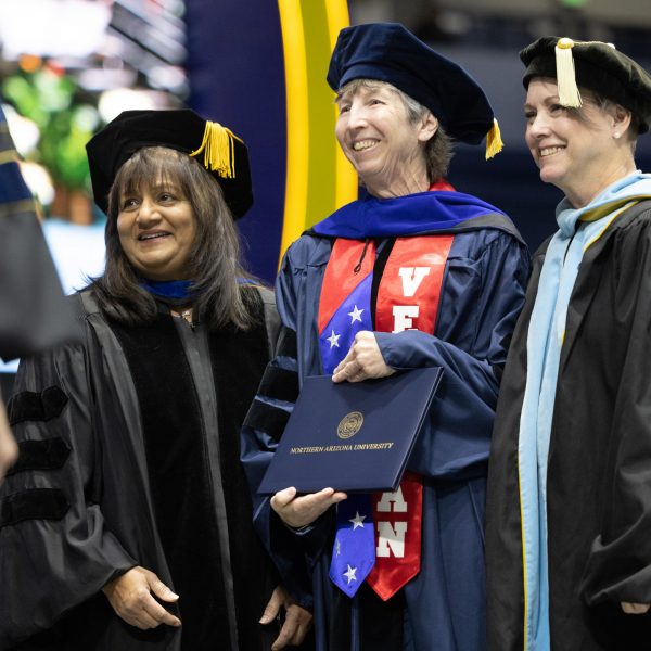 Rebecca Seeger with colleagues at commencement. They are in commencement regalia and Seeger is holding her graduation certificate.