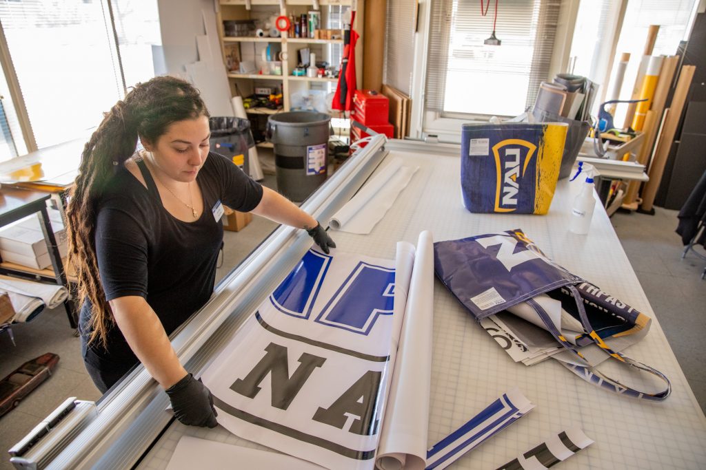 Sara LaRosa measures an NAU banner on a worktable.