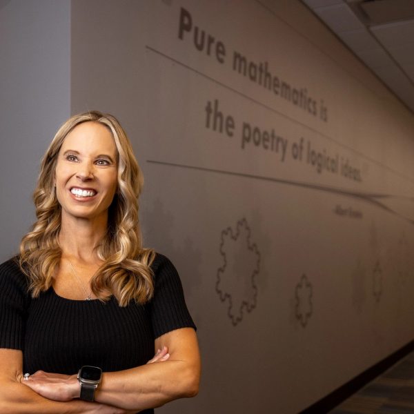 Mathematics Associate Professor Angie Hodge-Zickerman stands by wall in math lab that reads: "Pure mathematics is the poetry of logical ideas."