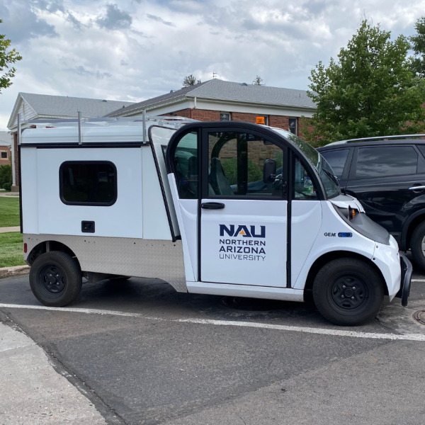 A parked white Electric Utility Vehicle (EUV) with the logo N A U Northern Arizona University on the door and a utility shell on the back for storing tools.