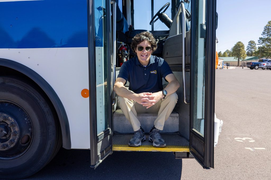 Information Systems major, Daniel Solis sitting on the entry steps for an NAU shuttle.