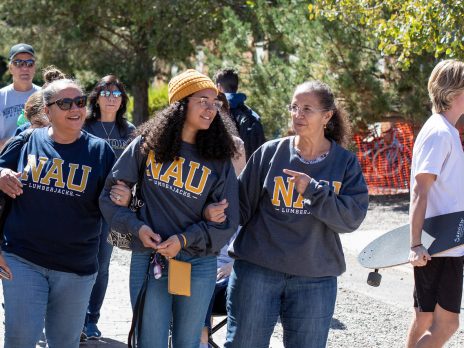 A smiling family walks together on the sunny Flagstaff campus wearing "NAU" sweatshirts