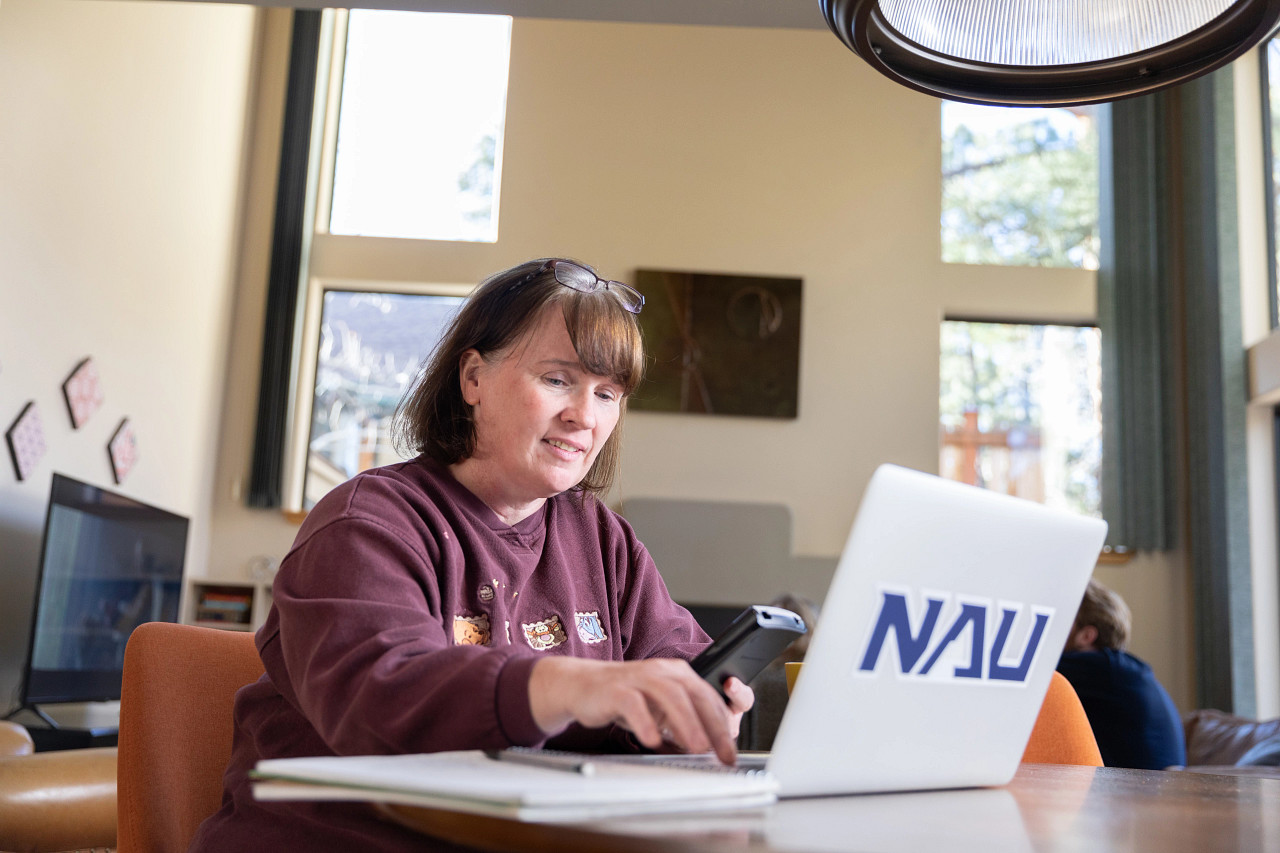A woman working on her laptop with a large NAU sticker.