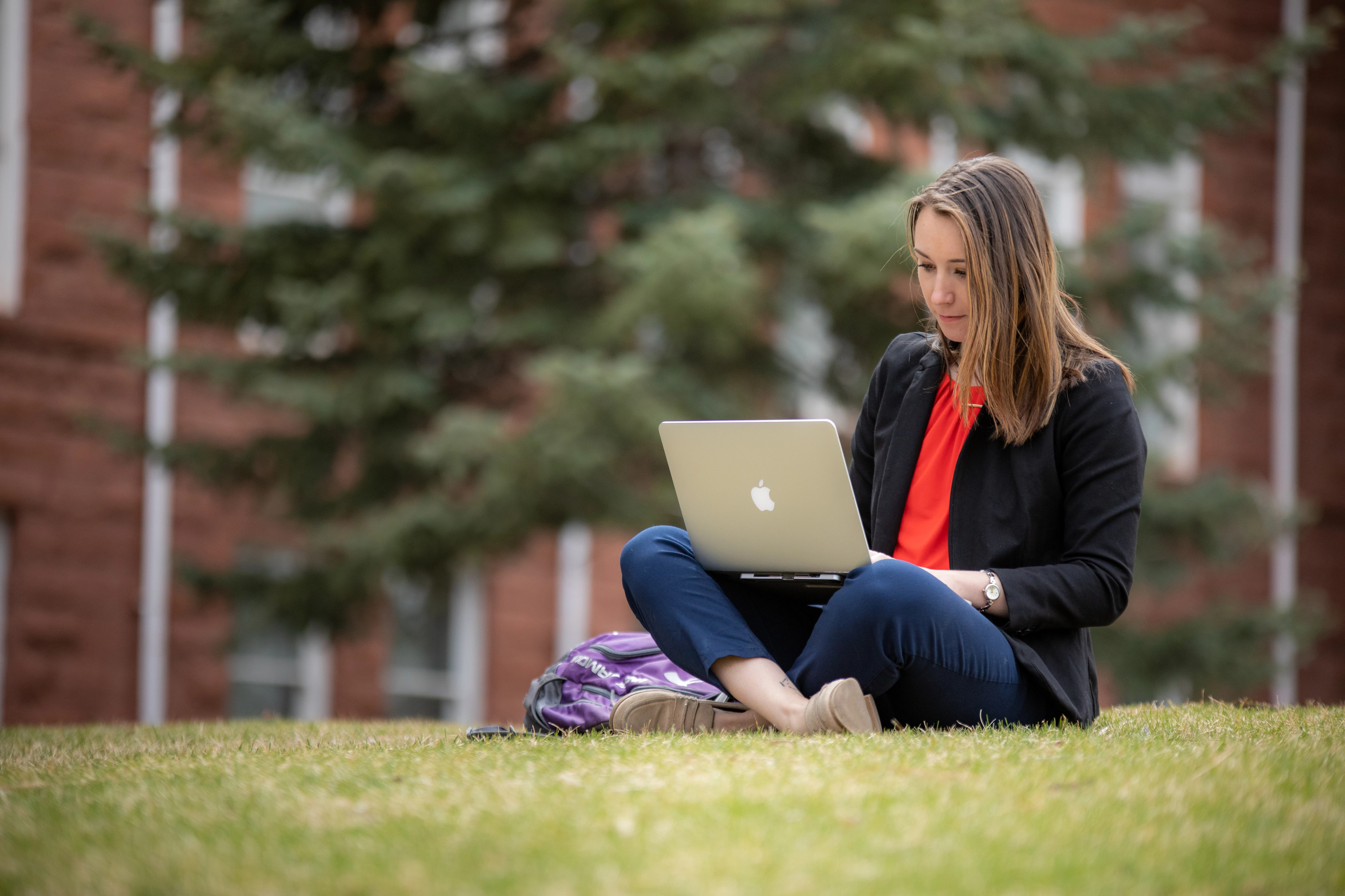 A student sitting on the grass working on her laptop.