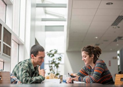 Two NAU students smile while studing together at a table.