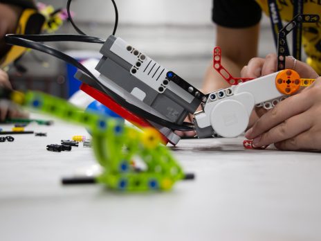 Youths are shown close up playing with a lego robot. 