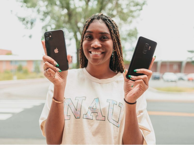 Student holds up an Apple and Android phone smiling.