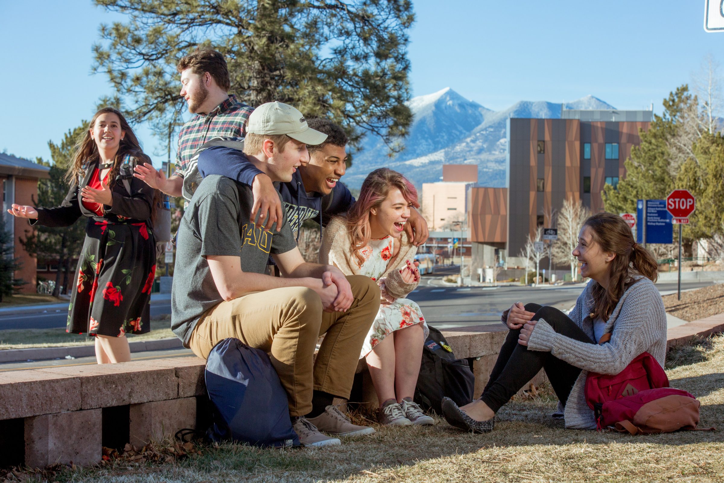 A group of friends hanging out together outside with campus buildings and mountains in the background.