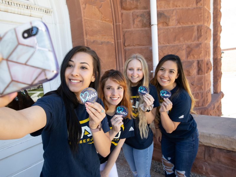 NAU students take selfie while holding stickers and smiling