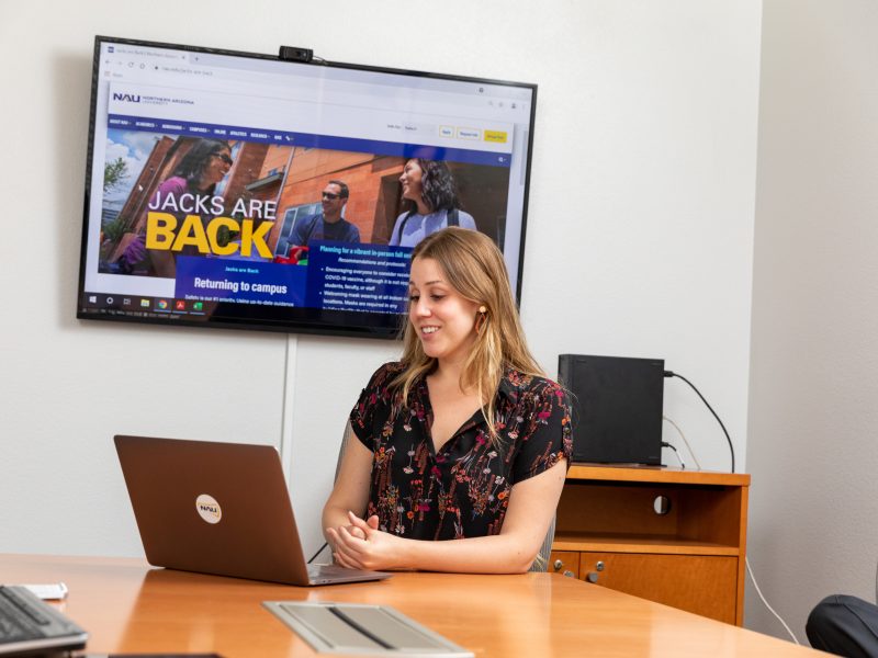 NAU University Marketing staff sits in front of a TV on her laptop