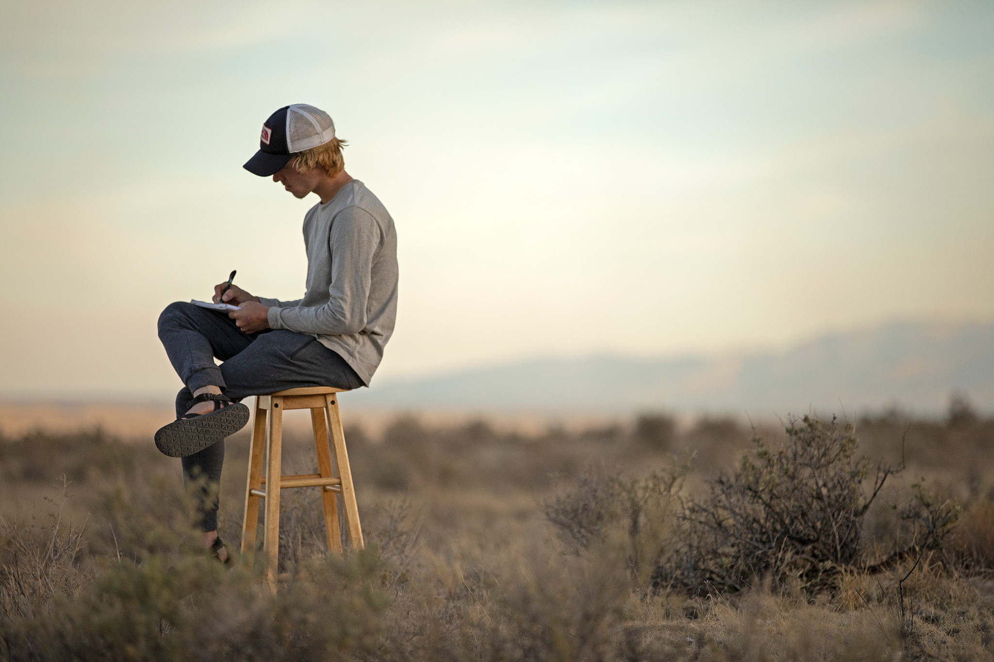 Student writes in a journal while sitting on a stool in a field