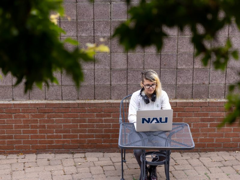 A student types on her laptop while sitting at a table outside.