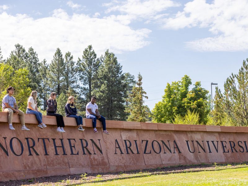 South N A U campus sign with students sitting on top of it.